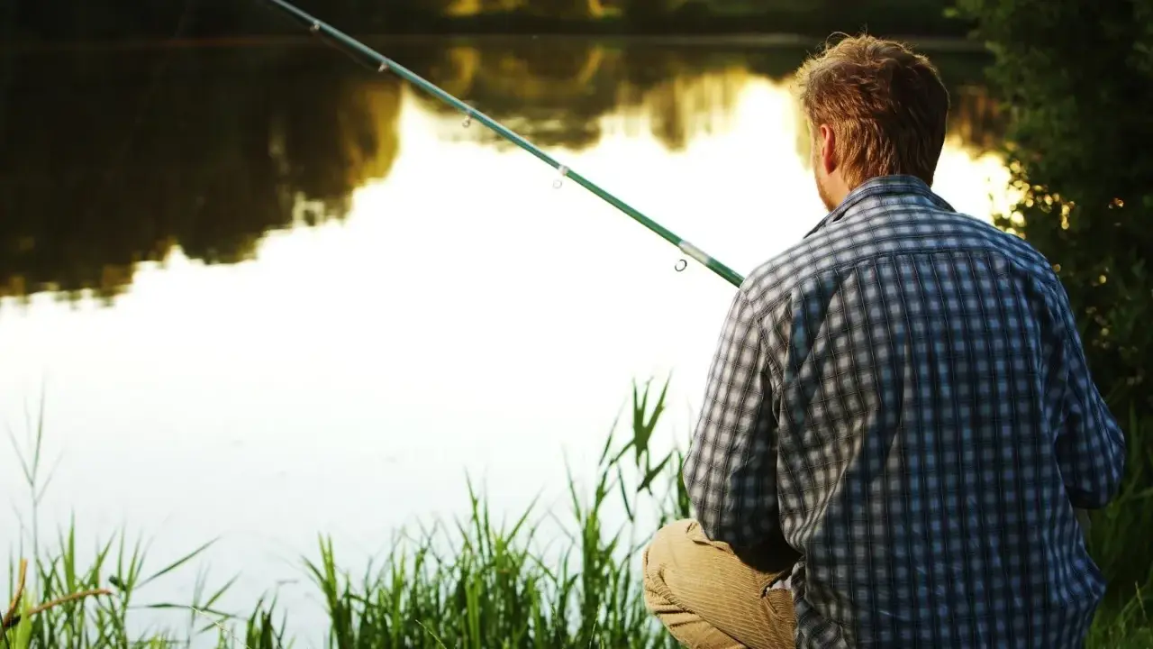 Mężczyzna w kratę łowi ryby na spokojnym łowisku. Słońce odbija się w wodzie, tworząc magiczną atmosferę.