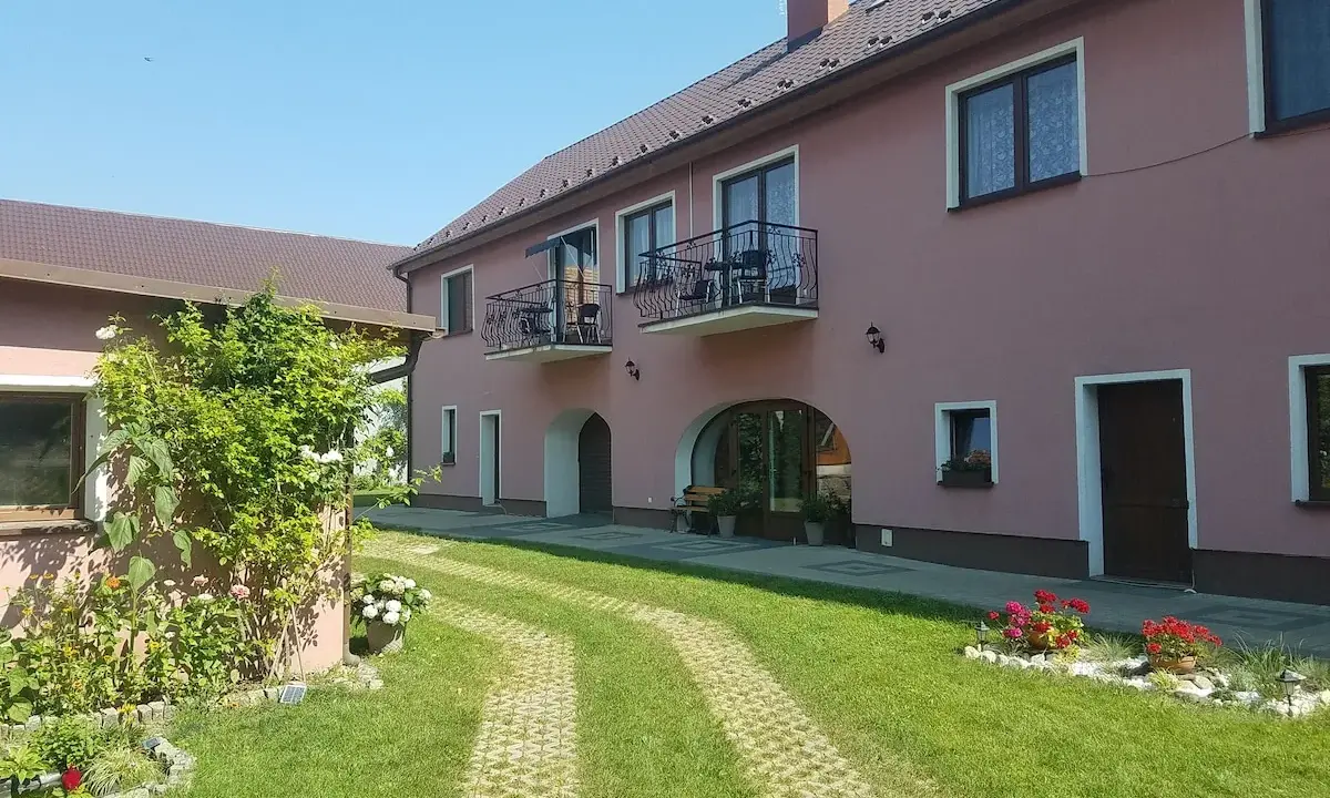 Urokliwe łowisko Trzeboszowice. Różowy budynek z balkonami, zielony ogród i ścieżka z kostki brukowej.