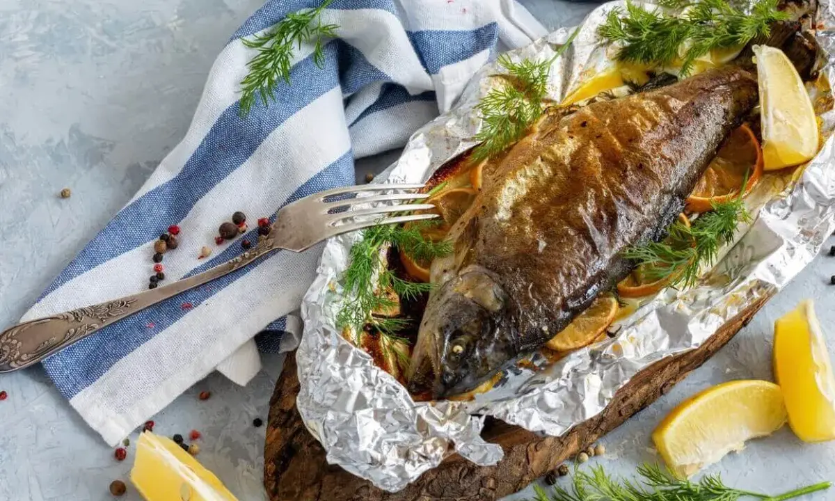 Pieczony pstrąg hodowlany w folii, podany z cytryną i koperkiem. Apetyczny posiłek gotowy do spożycia.