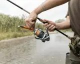 Wędkarz przygotowuje się do łowienia na rosówki, trzymając spinning i przynętę.