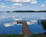Drewniany pomost na spokojnych jeziorach w mazowieckim, odbijających błękitne niebo z chmurami.