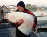 Szczęśliwy wędkarz trzyma ogromnego halibuta. Zapach halibut na jakie ryby - to pytanie zadaje sobie każdy, kto zobaczy ten okaz!