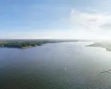 Widok na rozległy zalew zemborzycki z lasem po lewej i zabudowaniami po prawej. Na wodzie widać żaglówki.