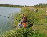 Wędkarz siedzi nad jeziorem, przygotowując się do łowienia. Czy to bat, czy inna wędka, ważne, że relaks nad wodą.