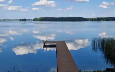 Drewniany pomost na spokojnych jeziorach w mazowieckim, odbijających błękitne niebo z chmurami.