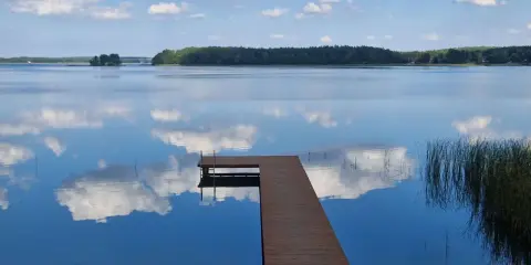Drewniany pomost na spokojnych jeziorach w mazowieckim, odbijających błękitne niebo z chmurami.