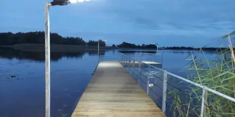 Drewniany pomost nad jeziorem, oświetlony lampami, zaprasza do wieczornego spaceru. Czy pomost nad jeziorem może być prywatny?