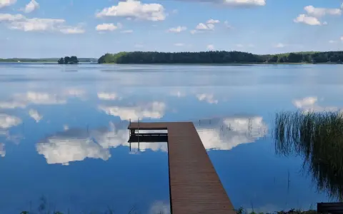 Drewniany pomost na spokojnych jeziorach w mazowieckim, odbijających błękitne niebo z chmurami.