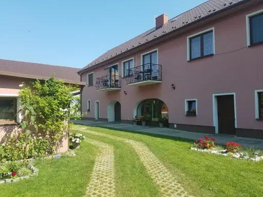 Urokliwe łowisko Trzeboszowice. Różowy budynek z balkonami, zielony ogród i ścieżka z kostki brukowej.