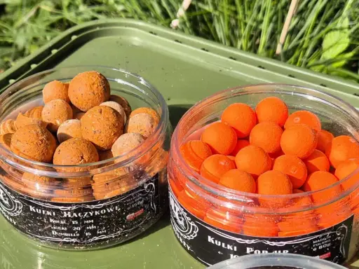 Dwa słoiczki z przynętami wędkarskimi: po lewej brązowe kulki haczykowe, po prawej pomarańczowe kulki pop-up. Idealne na karpia, w tym **dumbbells** na karpia.
