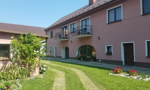 Urokliwe łowisko Trzeboszowice. Różowy budynek z balkonami, zielony ogród i ścieżka z kostki brukowej.
