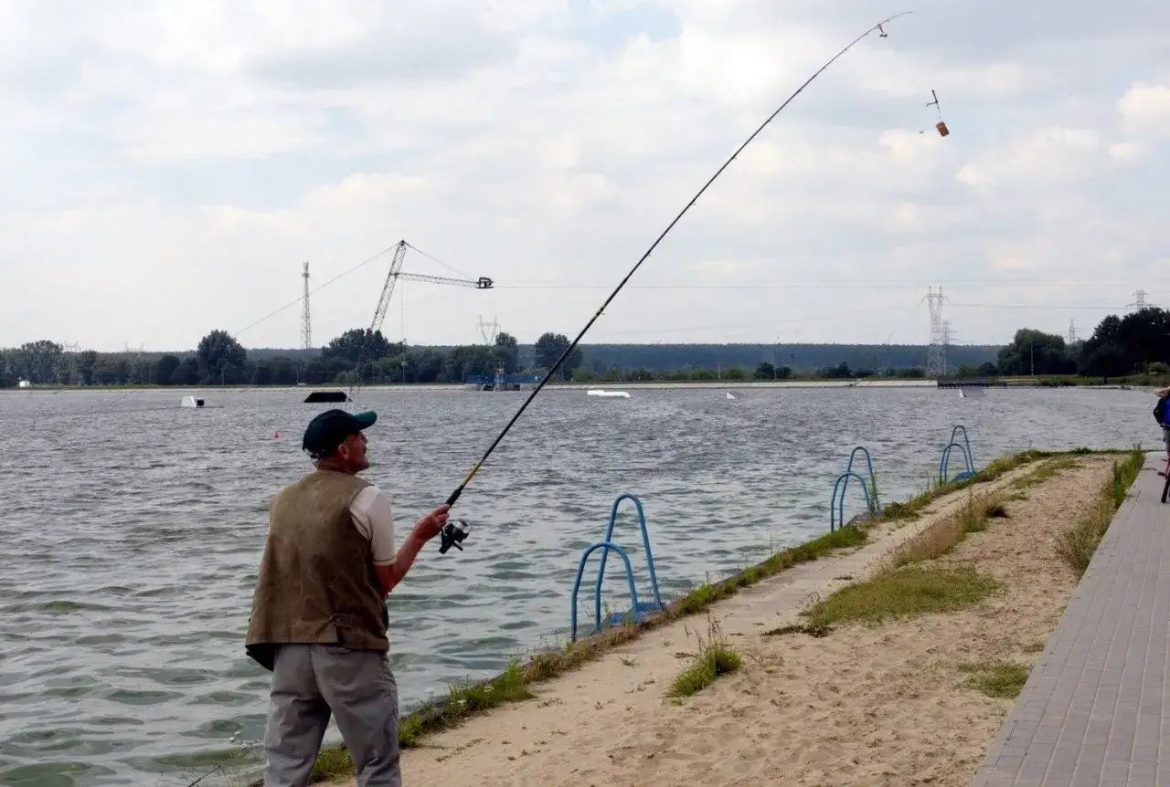 Wędkarz łowi ryby nad zalewem zemborzyckim. W tle widać wieżę wyciągu do wakeboardu.