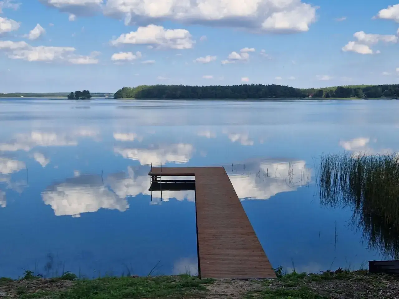 Drewniane molo na spokojnych jeziorach w mazowieckim, odbijających błękitne niebo z białymi chmurami.